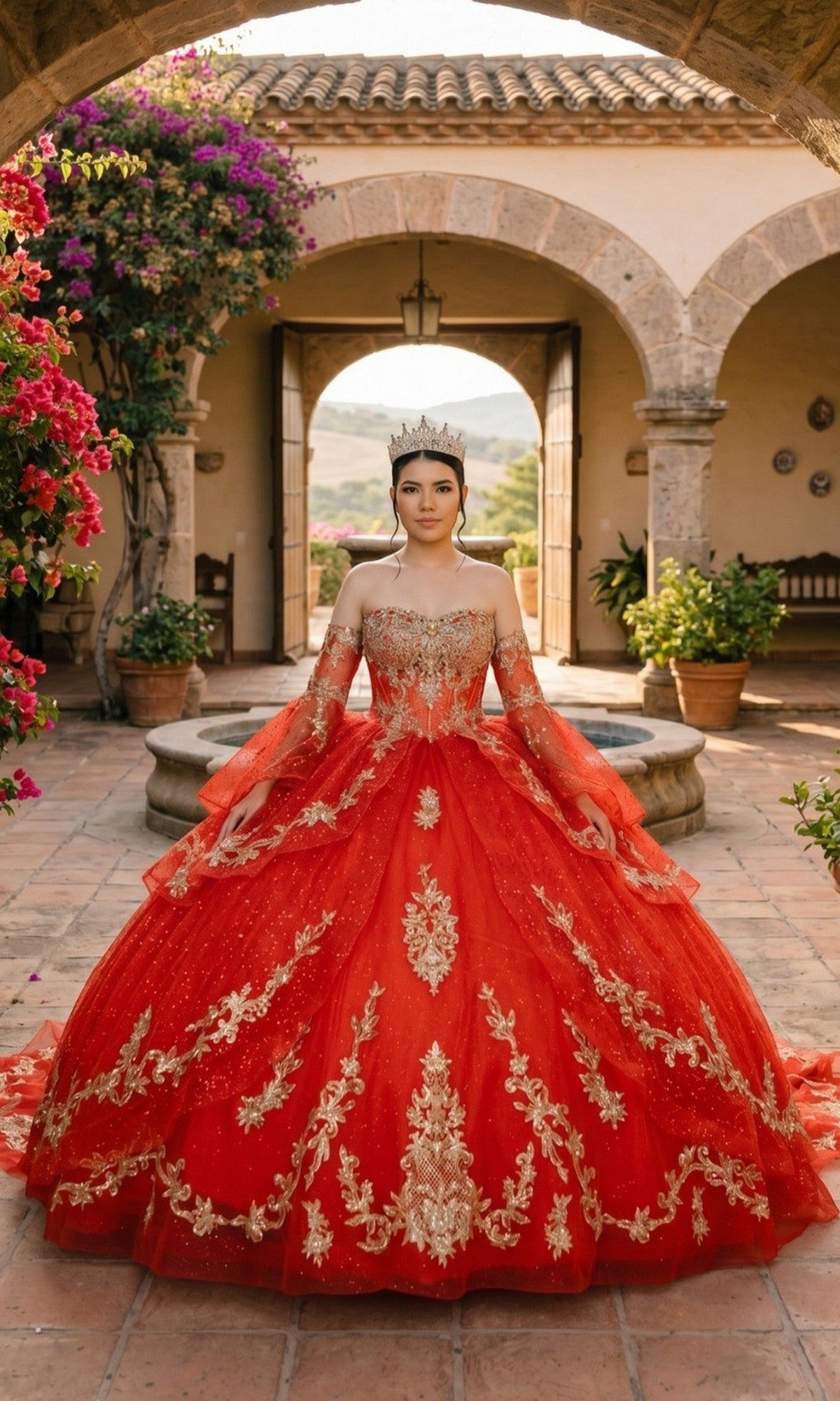 A woman in the red Quinceanera Dress 8575JQ by Cinderella Couture stands in a courtyard adorned with flowers and archways, with mountain views in the background, wearing a crown.